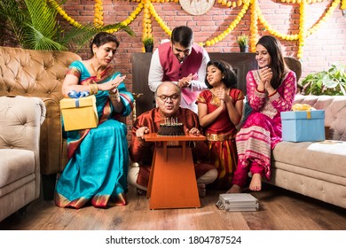 Indian old man with Family celebrating birthday by blowing candles on cake while wearing ethnic wear - Powered by Shutterstock