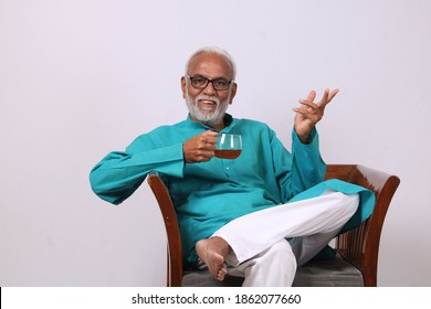 Indian old man having green tea while sitting on chair.