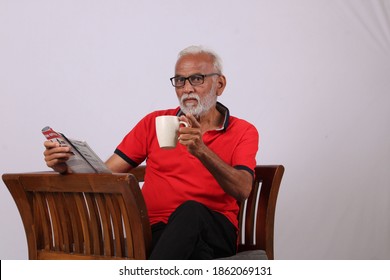 Indian Old Man Reading Magazine While Sitting On Chair With A Coffee Mug.