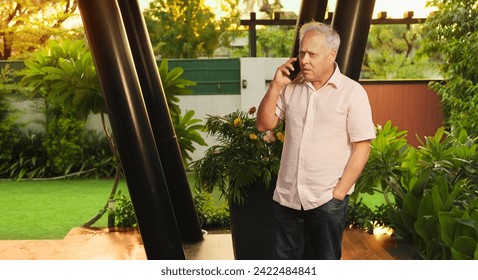 Indian old upset sad unhappy senior man standing outdoor house park talking on mobile phone. Worried alone middle aged older grandfather using smartphone hearing awful news about business failure  - Powered by Shutterstock