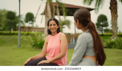 Indian older relax confident healthy woman with beautiful cute teenager girl sitting on mat talk gossip about warm up workout exercise during break time enjoy spend time together outdoor home garden - Powered by Shutterstock