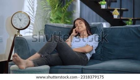 Indian peaceful teen girl sitting leaning on comfortable sofa daydreaming breathing fresh air conditioned in living room. Happy beautiful dreamy female resting alone distance think plan or visualize 