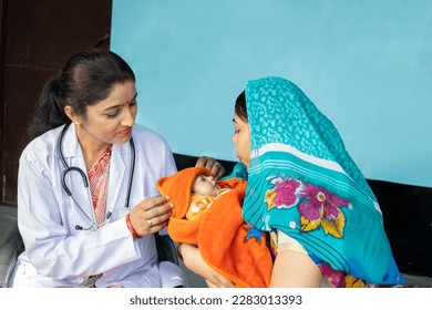 Indian pediatrician doctor examine new born baby at village, Mother wearing sari get infant check by medical person. Rural healthcare camp concept. - Powered by Shutterstock