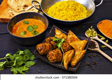 Indian pilau rice in balti dish served with chicken tikka masala curry, plain naan bread, vegetable samosas, and onion bhajis