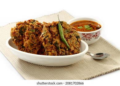 Indian Popular Snack Called Palak Vada Or Spinach  Fritter In White Bowl  Souse Called Chana Rassa In Bowl And Green Chilli With Spoon On Dinning Matte 