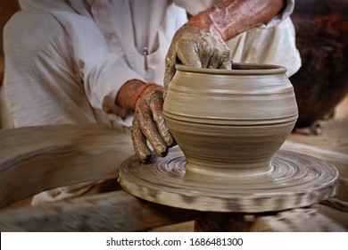 Indian potter at work: throwing the potter's wheel and shaping ceramic vessel and clay ware: pot, jar in pottery workshop. Experienced master. Handwork craft from Shilpagram, Udaipur, Rajasthan, India - Powered by Shutterstock