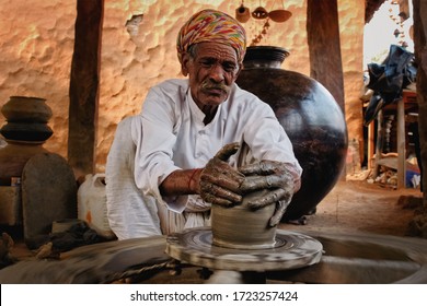 Indian potter at work: throwing the potter's wheel and shaping ceramic vessel and clay ware: pot, jar in pottery workshop. Experienced master. Handwork craft from Shilpagram, Udaipur, Rajasthan, India - Powered by Shutterstock