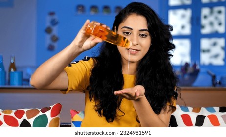 Indian pretty woman with perfect skin taking hair oil from the bottle - beauty concept. Closeup shot of a lady with long curly hair taking oil from the bottle in her hands - aroma oil therapy - Powered by Shutterstock