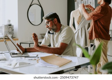 Indian professional designer discussing details with customer via smartphone while tailor creating new dress - Powered by Shutterstock