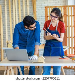 Indian Professional Male Engineer Foreman Labor Worker Using Laptop Computer Meeting Discussing With Cheerful Female Colleague Wear Safety Goggles Writing Note On Paper Clipboard In Construction Site.