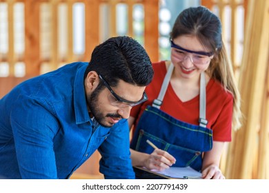 Indian Professional Male Engineer Foreman Labor Worker Using Laptop Computer Meeting Discussing With Cheerful Female Colleague Wear Safety Goggles Writing Note On Paper Clipboard In Construction Site.