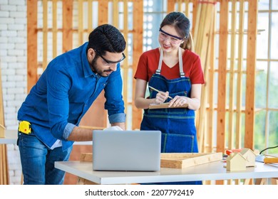 Indian Professional Male Engineer Foreman Labor Worker Using Laptop Computer Meeting Discussing With Cheerful Female Colleague Wear Safety Goggles Writing Note On Paper Clipboard In Construction Site.