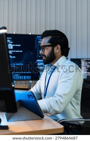 Indian programmer typing on keyboard, programming software code and managing network server database dashboard on computer monitor screen at night