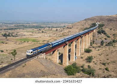 Indian railways long passenger train, exiting a tunnel to cross a tall railway bridge. - Powered by Shutterstock