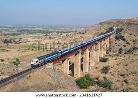 Indian railways long passenger train, exiting a tunnel to cross a tall railway bridge.