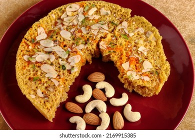 Indian Rajasthani Crunchy Sweet Dish  Called Ghevar Or Ghewar Is An  Made Using Refined Flour, Sugar, And Ghee. Garnished With Silver Foil And Dry Fruits In Dark Maroon Dish, Selective Focus