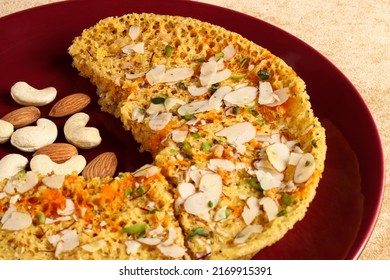 Indian Rajasthani Crunchy Sweet Dish  Called Ghevar Or Ghewar Is An  Made Using Refined Flour, Sugar, And Ghee. Garnished With Silver Foil And Dry Fruits In Dark Maroon Dish, Selective Focus