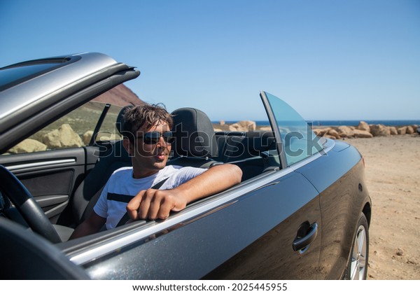 Indian rich man sitting in\
his convertible car wears sunglasses and looks to the side.\
Realized man sitting in an expensive car. Forty year old person of\
indian ethnicity