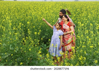 Indian Rural Happy Family From A Farmer Family Looking Into The Phone In Village In A Mustard Field In A Green Farm Yellow Flowers Happy In Flourishing Crops.