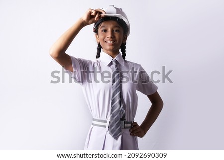 Indian Rural kid preparing herself to become an engineer in future. The rural girl is holding an engineering helmet portraying child education and grooming concept.