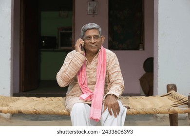 Indian rural old man talking on mobile at home - elder villager using phone - Concept of senior rural people using technology and smartphone - Powered by Shutterstock