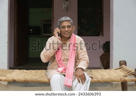 Indian rural old man talking on mobile at home - elder villager using phone - Concept of senior rural people using technology and smartphone