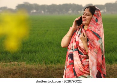 Indian rural woman villager farmer talking on a mobile phone in a mustard field in a green farm in natural environment. - Shutterstock ID 2028790022