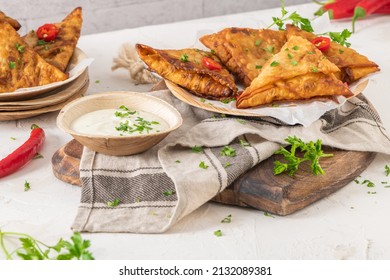 Indian samosas - fried or baked pastry with savoury filling, popular Indian snacks, served with yogurt sauce in areca leaf dishes with spices on kitchen countertop - Shutterstock ID 2132089381