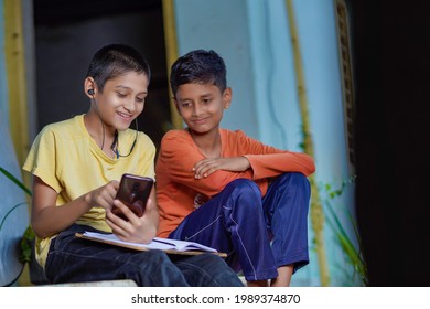 Indian School Boy Holding Phone Distance Learning Class Using Mobile Application, Watching Online Lesson, Video Calling In App Making Notes Studying At Home