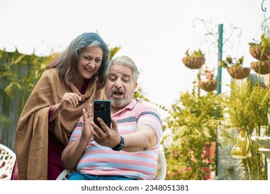 Indian senior couple using smartphone at home garden - Powered by Shutterstock