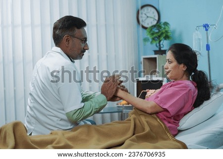 Indian senior doctor giving confidence to sick admitted woman on hospital bed by holding hands - concept of Healthcare support, Expert advice and Medical treatment