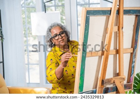 Indian Senior Female Artist Working On Painting In Studio on easel
