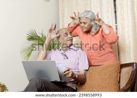 Indian senior woman teasing husband in living room , After retirement life enjoyment