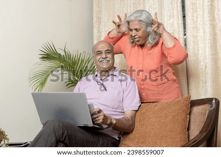 Indian senior woman teasing husband in living room , After retirement life enjoyment