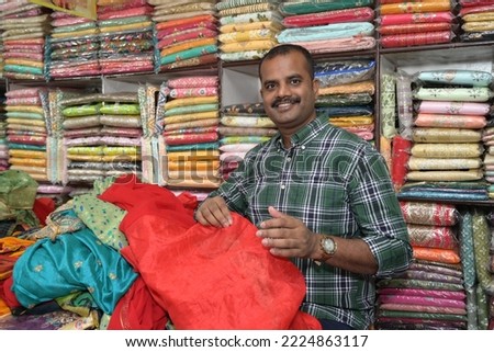 An Indian shopkeeper showing clothes from his store