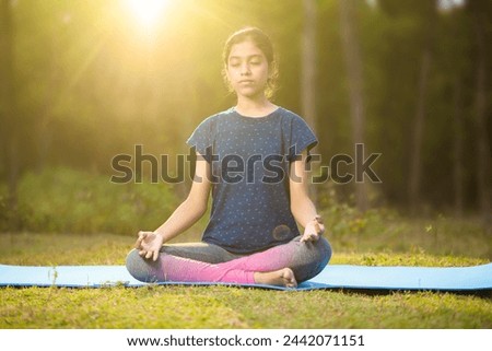 indian slim athlete girl sitting in a zen-like pose or padmasana position practicing yoga with gyana mudra in a peaceful nature