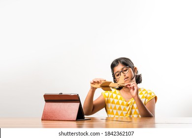 Indian Small Girl Student Making Or Measuring Wings Of Paper Plane Or Aeroplane, Doing School Project Or Learning Science With Online Tutorial