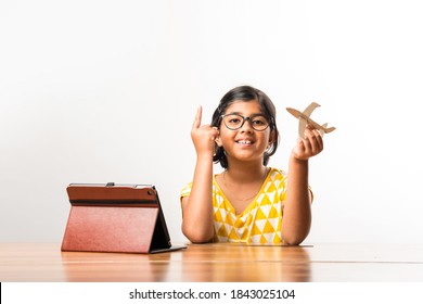 Indian Small Girl Student Making Or Measuring Wings Of Paper Plane Or Aeroplane, Doing School Project Or Learning Science With Online Tutorial