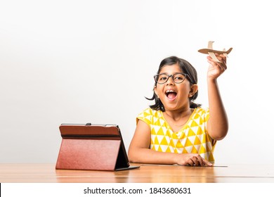 Indian Small Girl Student Making Or Measuring Wings Of Paper Plane Or Aeroplane, Doing School Project Or Learning Science With Online Tutorial