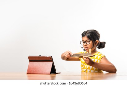 Indian Small Girl Student Making Or Measuring Wings Of Paper Plane Or Aeroplane, Doing School Project Or Learning Science With Online Tutorial