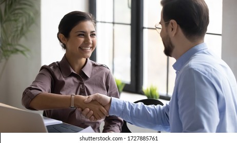 Indian smiling businesswoman shaking hands with man job seeker near laptop. Happy successful manager making deal with male partner using pc. Professional employee congratulations applicant.
