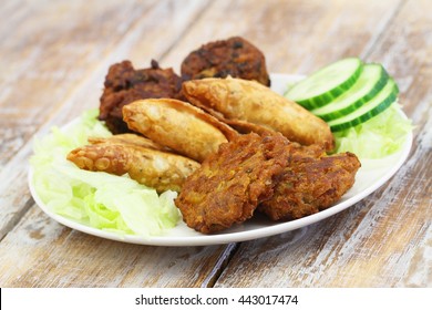Indian snacks including samosas, onion bhajis and pakoras on white plate on wooden surface
