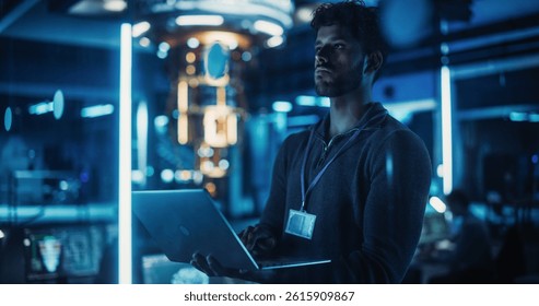 Indian Software Developer Standing in a Dark Modern Office, Working on a Laptop Computer. Young Diverse Specialist in Artificial Intelligence is Developing a Quantum Machine Learning Algorithm