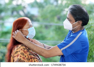 Indian Son Helping Old Mother Wearing Face Mask To Prevent Covid-19. Son Taking Care Of Old Mother During Corona Virus Pandemic. Teaching To Wear Mask Properly. How To Wear Face Mask.