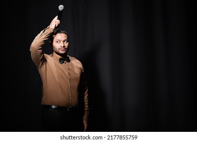 Indian Stand Up Comedian Holding Microphone On Head On Dark Stage On Black