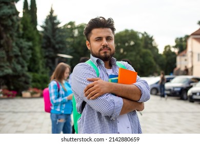 The indian student stands outdoors and holds a stack of books