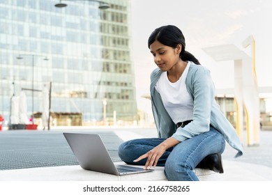 Indian Student Using Laptop Computer Studying, Watching Videos Sitting On Urban Street, Online Education Concept. Asian Woman Working Freelance Project Using Modern Technology, Copy Space  