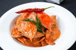 Indian Style Savory Crab Curry With Red Chili And Green Leaf On Top Served In A White Plate On A Black Background Eye Level Top View Mid Closeup.