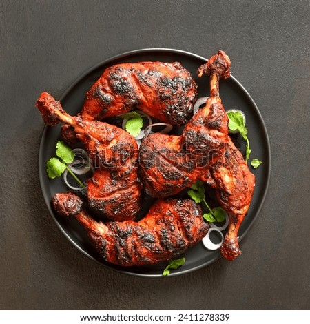 Indian style tandoori chicken on plate over dark stone background. Chicken legs marinated in yogurt and spices. Top view, flat lay