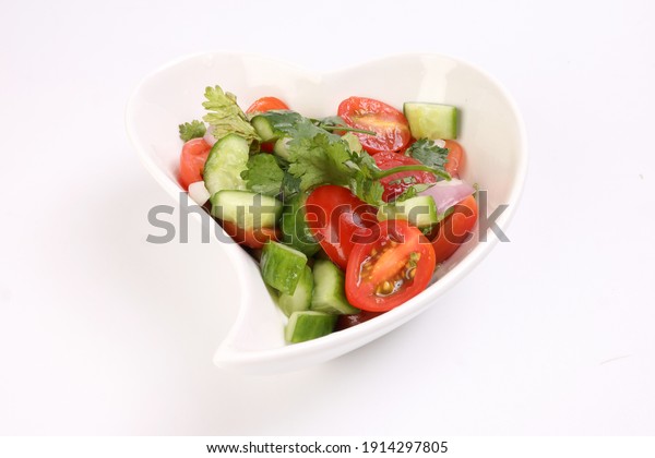 Indian\
Subcontinent style tomato cucumber onion chili coriander salad in\
hart shape white dish on white\
background